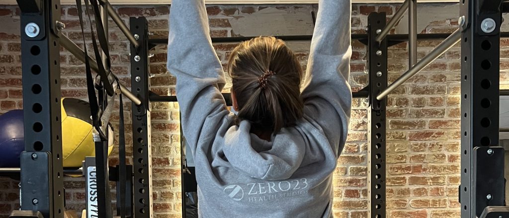 Vrouw in grijze trui doet pull-up aan rek in sportschool.