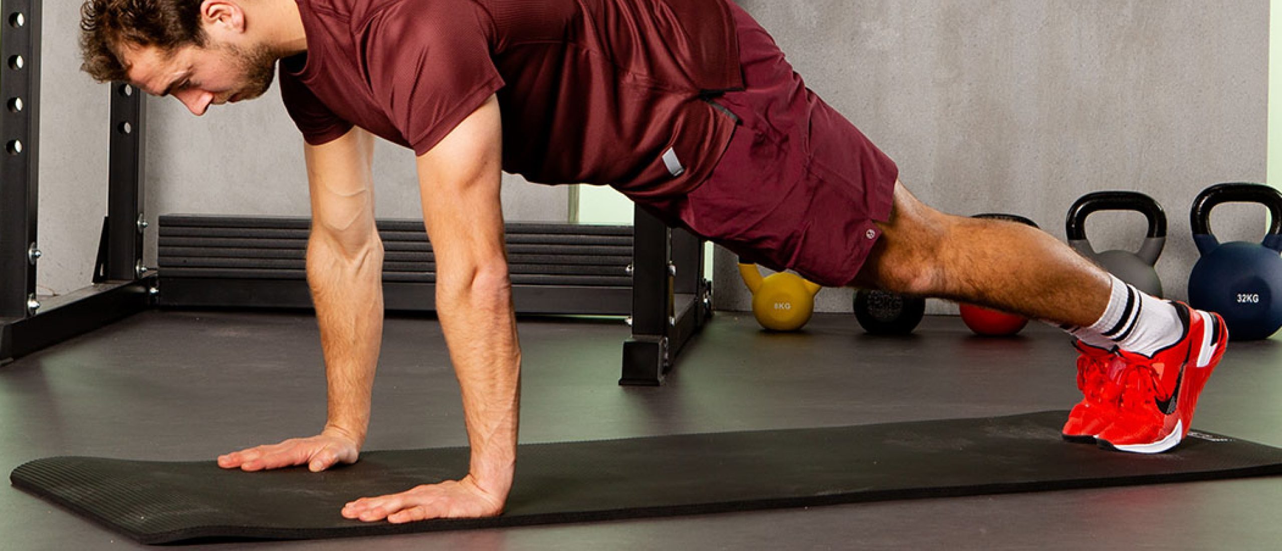 Man doet een plank in de sportschool op zwarte mat met rode schoenen.