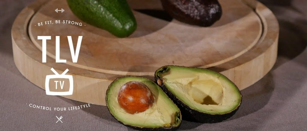 Halve avocado op houten bord met hele avocado ernaast.