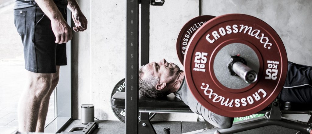 Man doet aan bankdrukken met rode halters in sportschool.