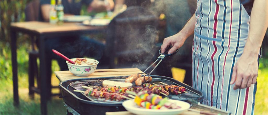Man grilt groentespiesjes en worstjes op barbecue.
