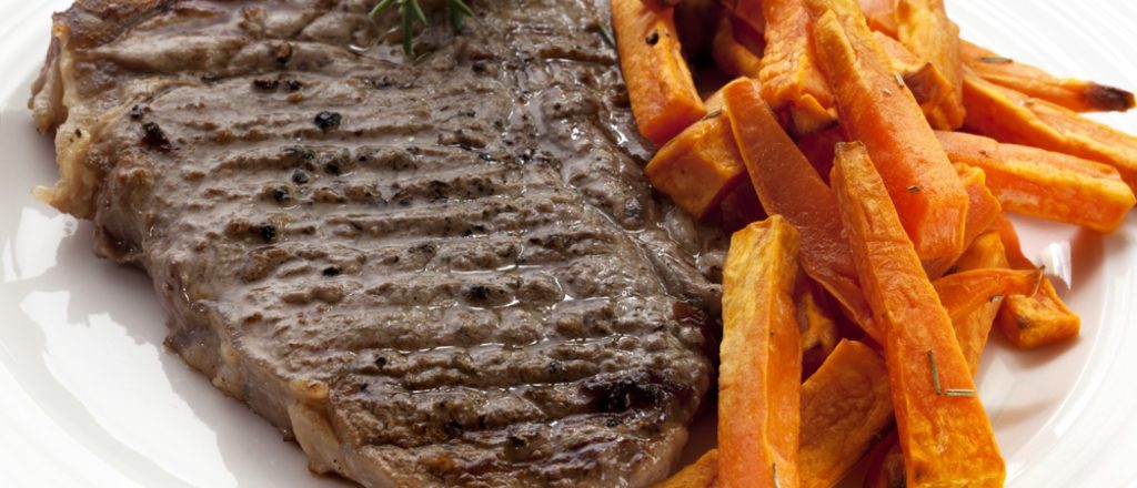 Gegrilde biefstuk met zoete aardappelfrietjes op bord.