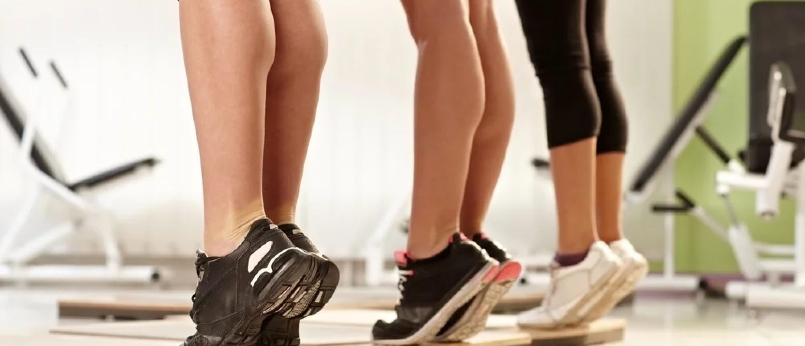 Algemene warming-up met stok voor je training 4 Drie personen strekken hun kuiten op een plankje in de sportschool.