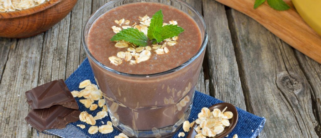 Glas met chocolade smoothie en havermout op houten tafel.