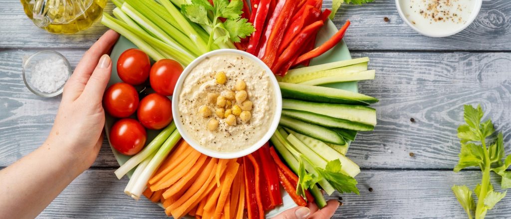 Schotel met groenten en hummus op houten tafel.