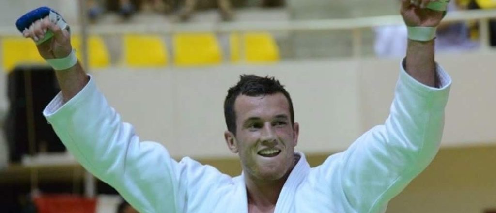 Man in judopak viert overwinning met armen omhoog.