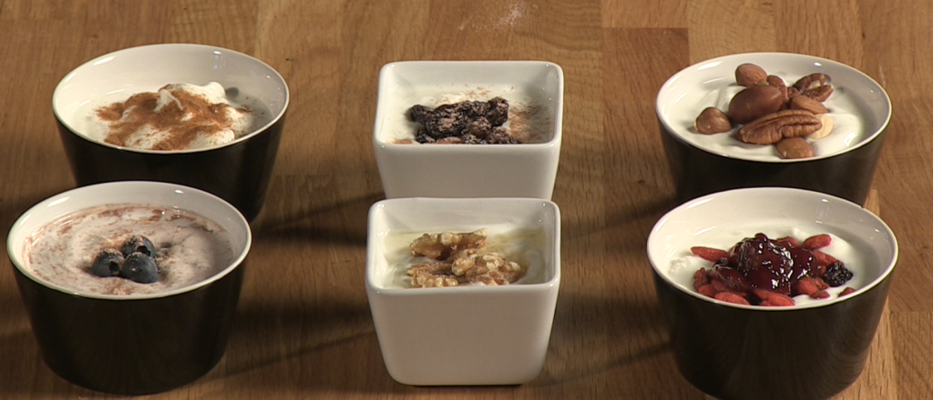 Zes kommen kwark met diverse toppings op houten tafel.