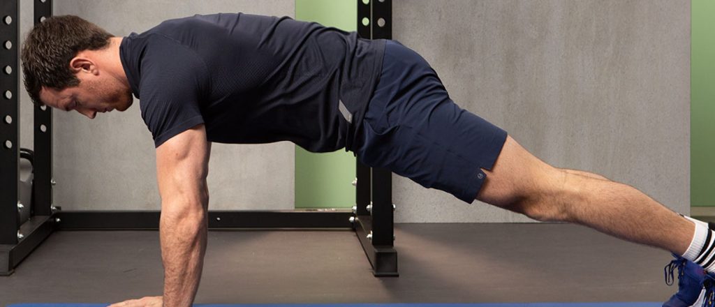 Man doet push-up op een blauwe mat in een gym.