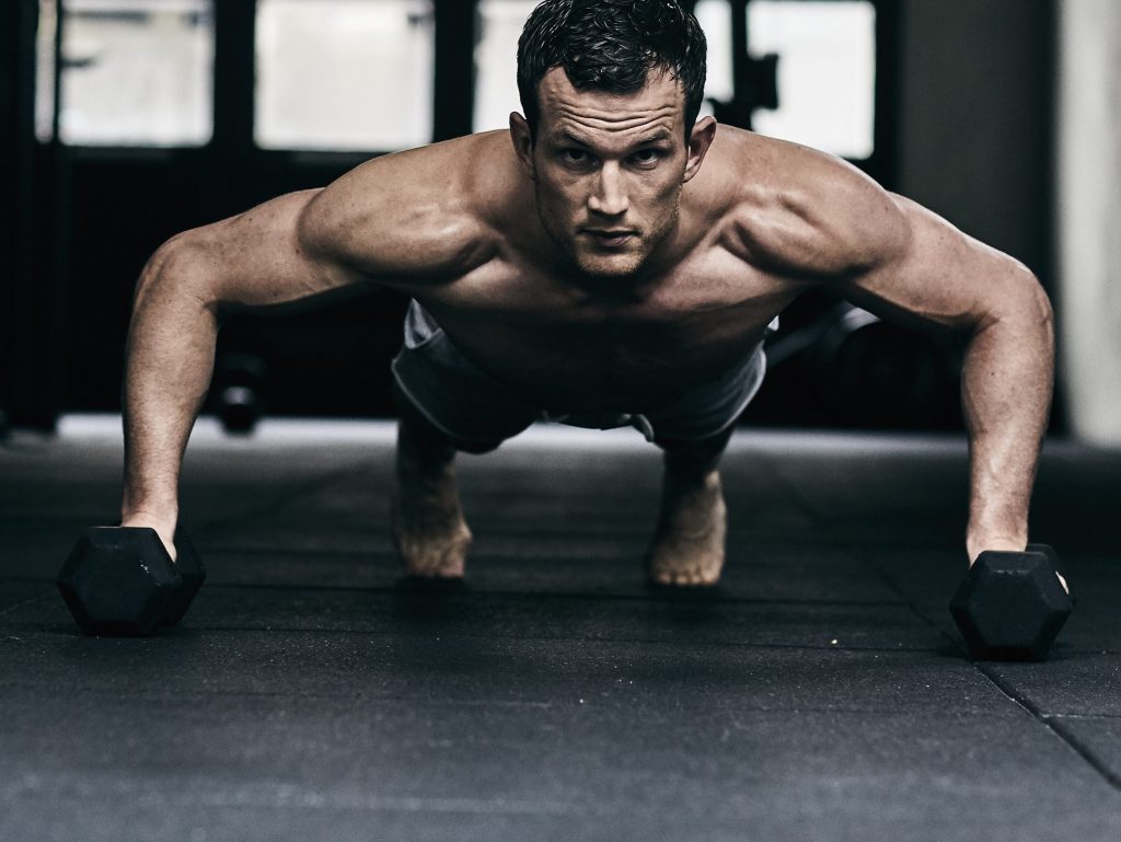 Man doet push-ups met dumbbells op de sportschoolvloer.