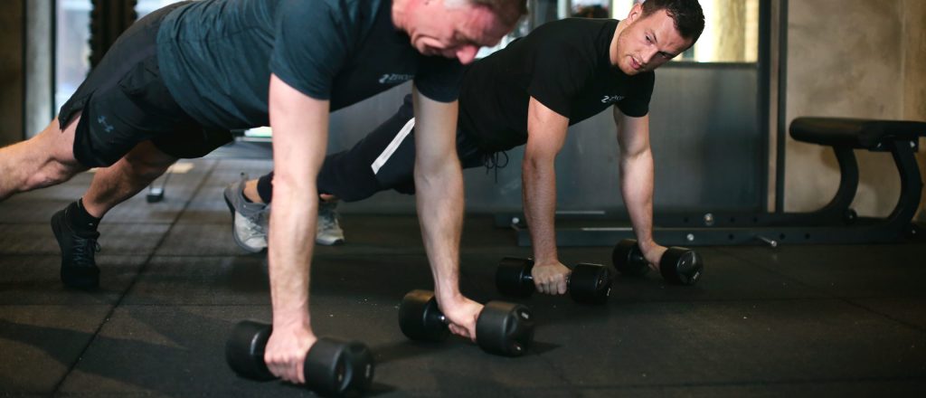 Twee mannen doen push-ups met dumbbells in de sportschool.