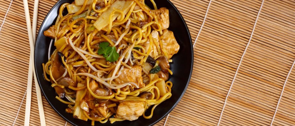 Een bord pad thai op een bamboemat met stokjes.