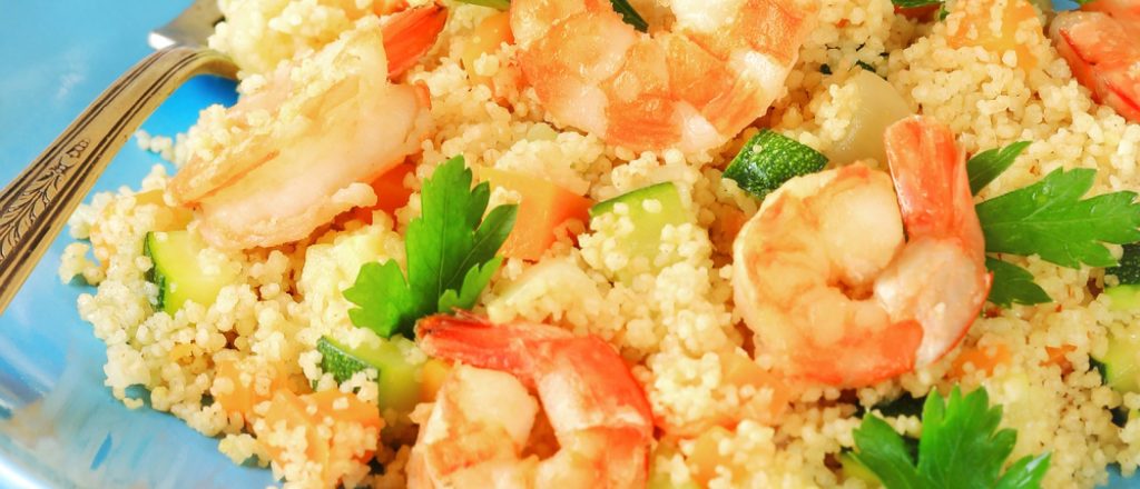 Parelcouscous met garnalen, groenten en peterselie op bord.