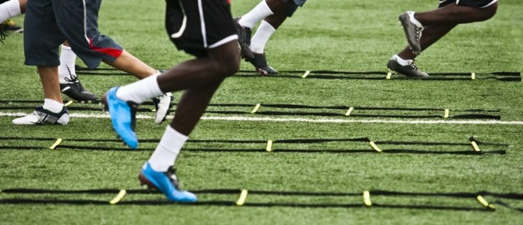 Mannen trainen met een speedladder op grasveld.