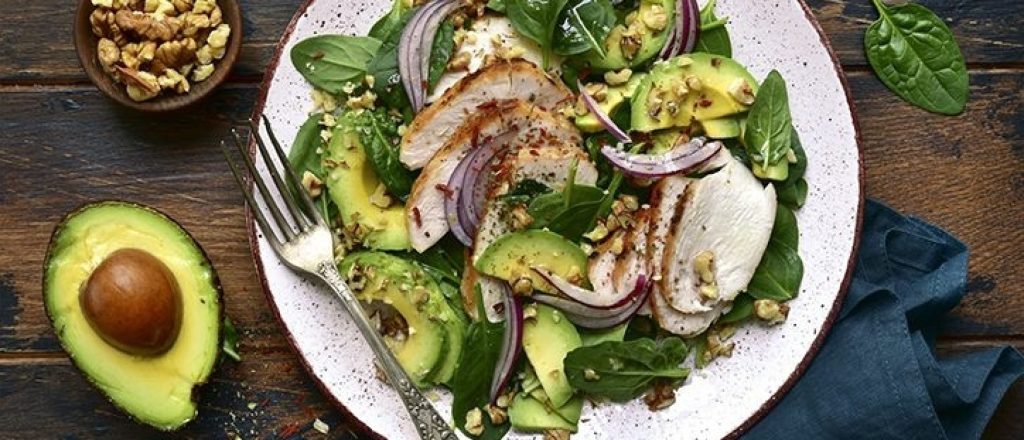 Salade met kip, avocado, spinazie en ui op bord.