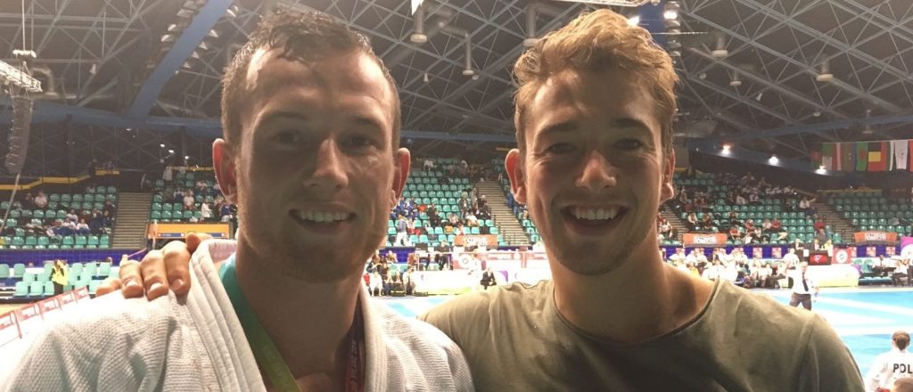 Twee mannen glimlachen in een overdekte sportarena.
