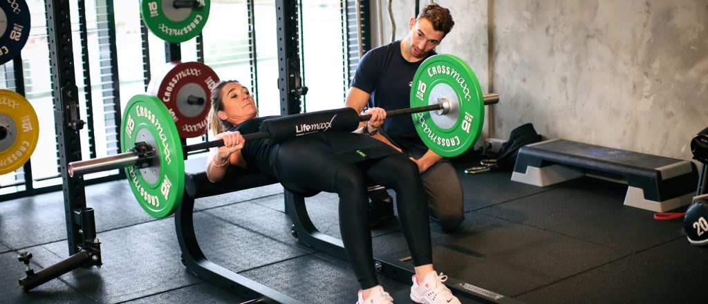 Vrouw doet oefening met barbell onder begeleiding in de sportschool.
