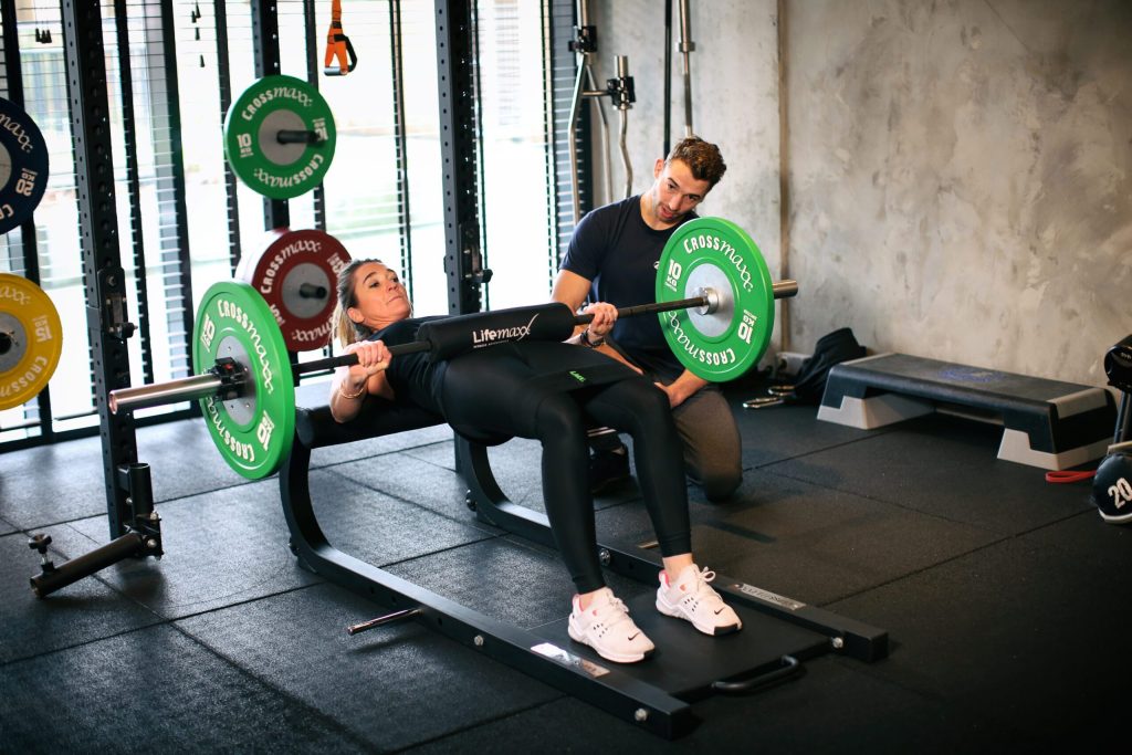 Vrouw doet barbell oefeningen in de sportschool met trainer erbij.
