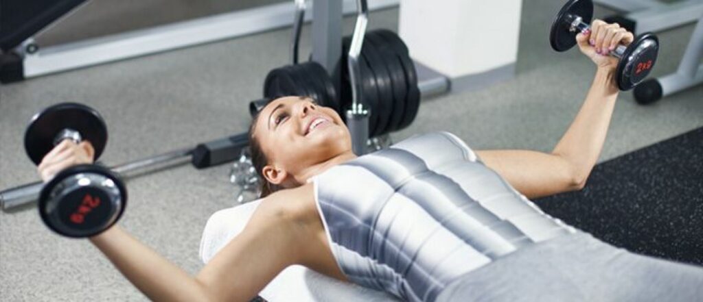 Vrouw ligt op een bank en doet dumbbell oefeningen