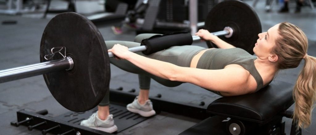 Vrouw voert een barbell hip thrust uit in de sportschool.