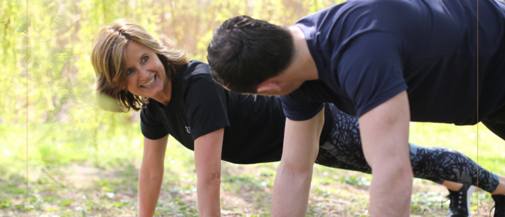 Man en vrouw doen push-ups buiten op het gras.