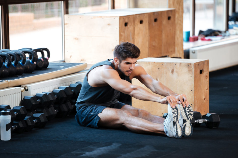 Hoe verminder je spierpijn na het sporten? 1 man stretching gym floor