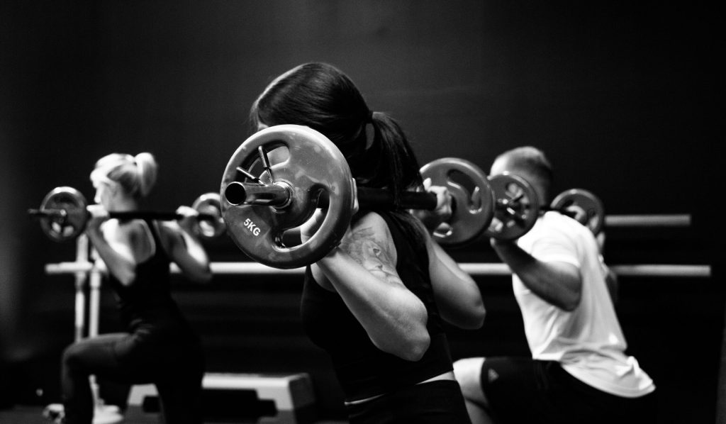 Drie mensen squatten met zware halters in een sportschool.