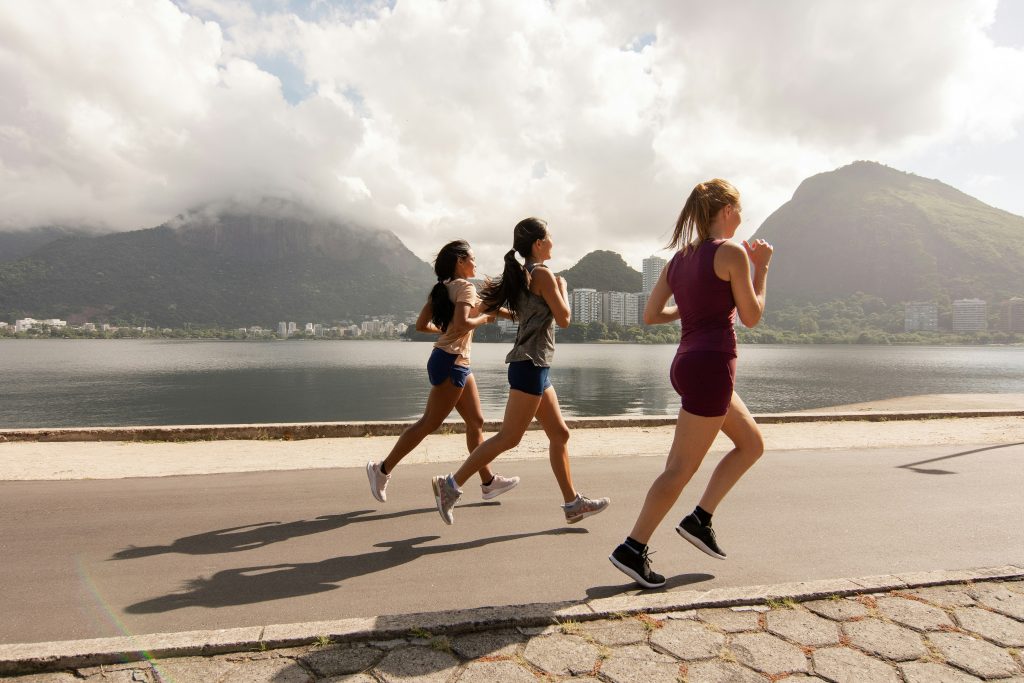 Drie vrouwen rennen langs een meer met bergen op de achtergrond.