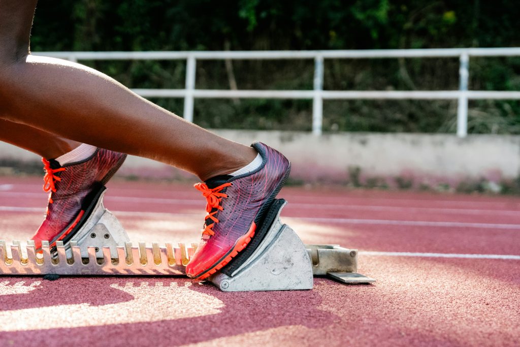 Atleet in startblok met rode schoenen op atletiekbaan.