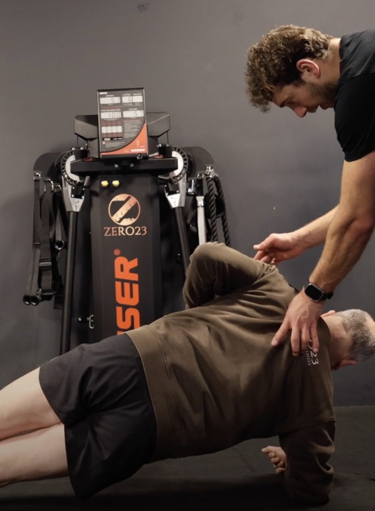 6 statische plank variaties 2 Man in plankpositie krijgt hulp van trainer in sportschool.