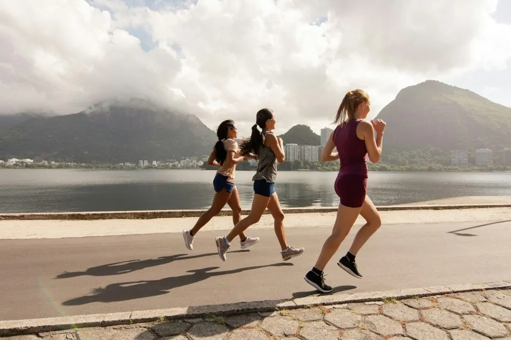Drie vrouwen rennen langs een meer met bergen op de achtergrond.